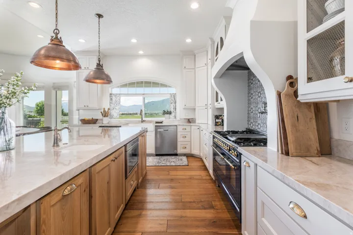 Gourmet kitchen featuring a large island with built-in microwave, wood-finish flooring, white cabinetry, integrated stainless steel dishwasher, and a professional-grade range with a custom range hood and patterned tile backsplash