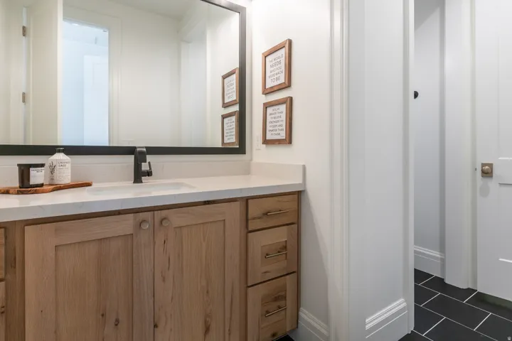 Bathroom vanity featuring a light wood-finish cabinet with storage, a white countertop, an undermount sink, and a black-finish faucet