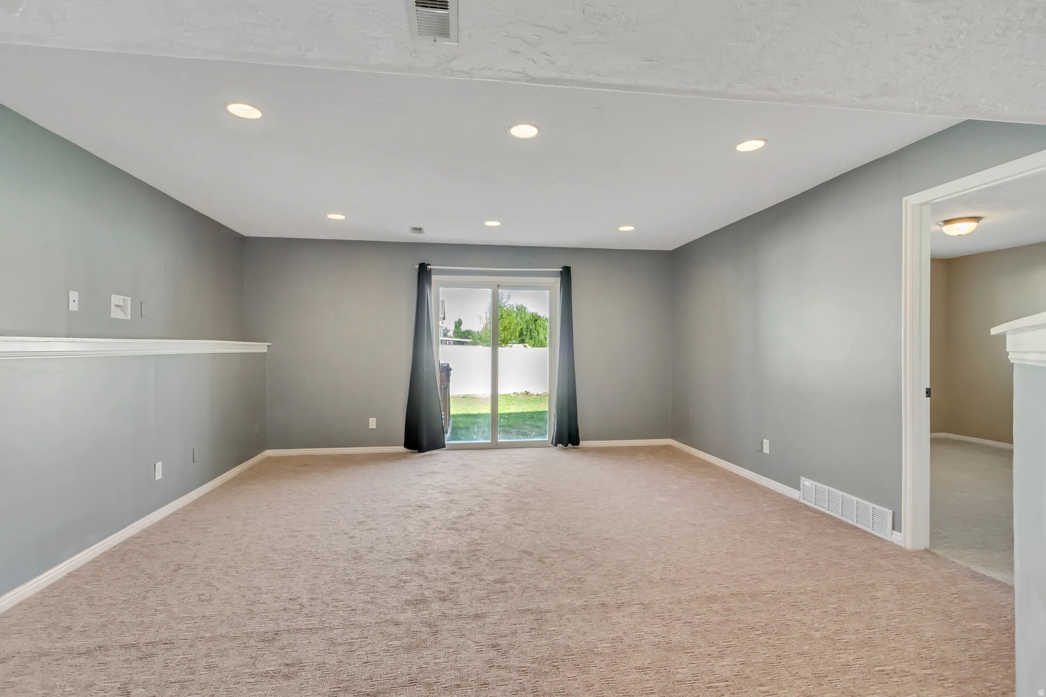 Carpeted room featuring recessed lighting, gray painted walls, white baseboards, and a glass sliding door providing access to the outdoors