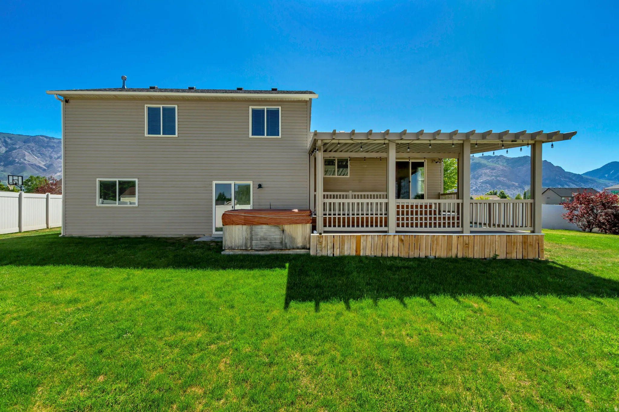 Rear exterior featuring a pergola-covered patio with string lighting, a hot tub, and a spacious lawn