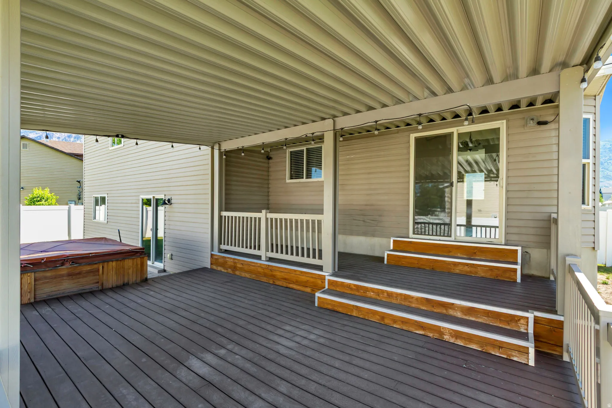 Expansive covered deck featuring composite decking, a built-in hot tub, and a sliding glass door entry