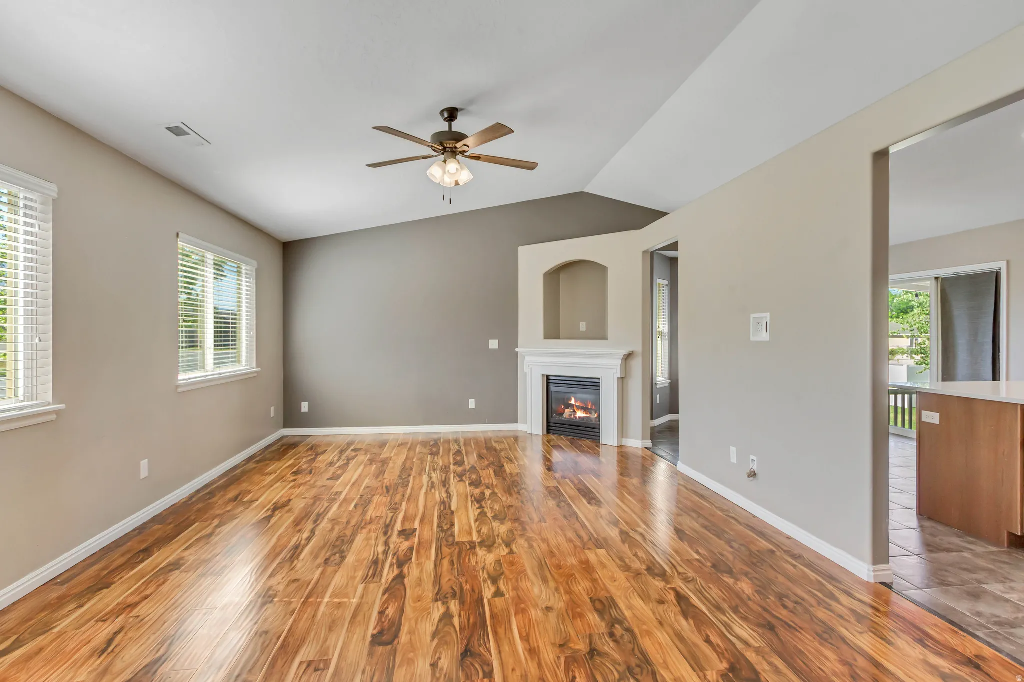 Living room featuring wood-finish flooring, a fireplace with a white mantel and arched alcove, vaulted ceiling, and a ceiling fan
