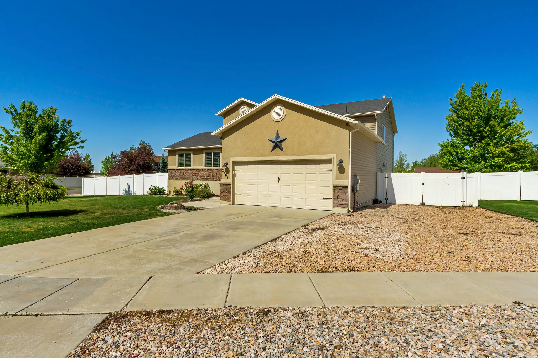 Stucco and stone facade home featuring an attached two-car garage with a panel door, a concrete driveway, and a white vinyl privacy fence enclosing the backyard