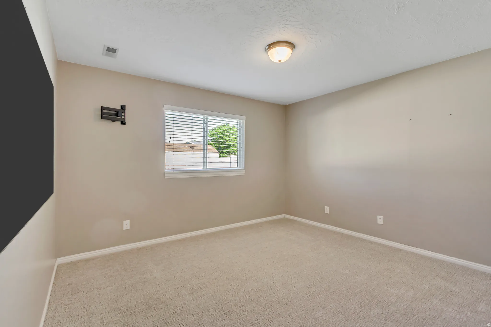 Carpeted room with neutral wall tones and a window featuring blinds