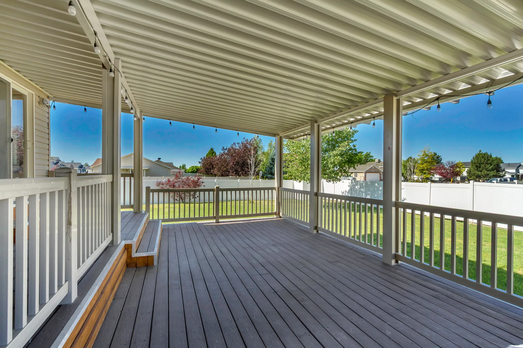 Spacious covered deck featuring composite decking, white railing, and a corrugated metal patio cover