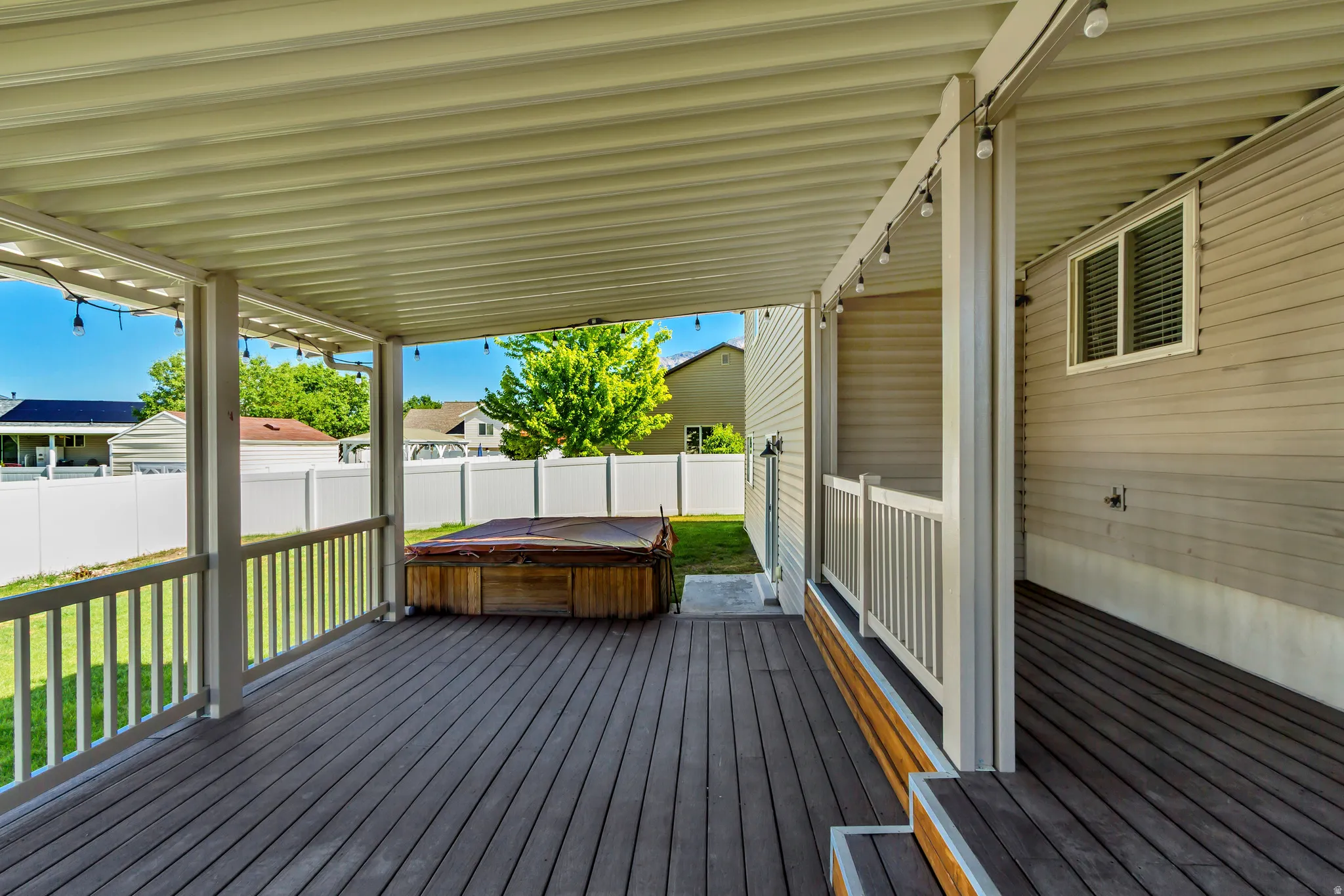 Expansive covered deck featuring composite decking, a built-in spa, white vinyl railing, and exterior lighting