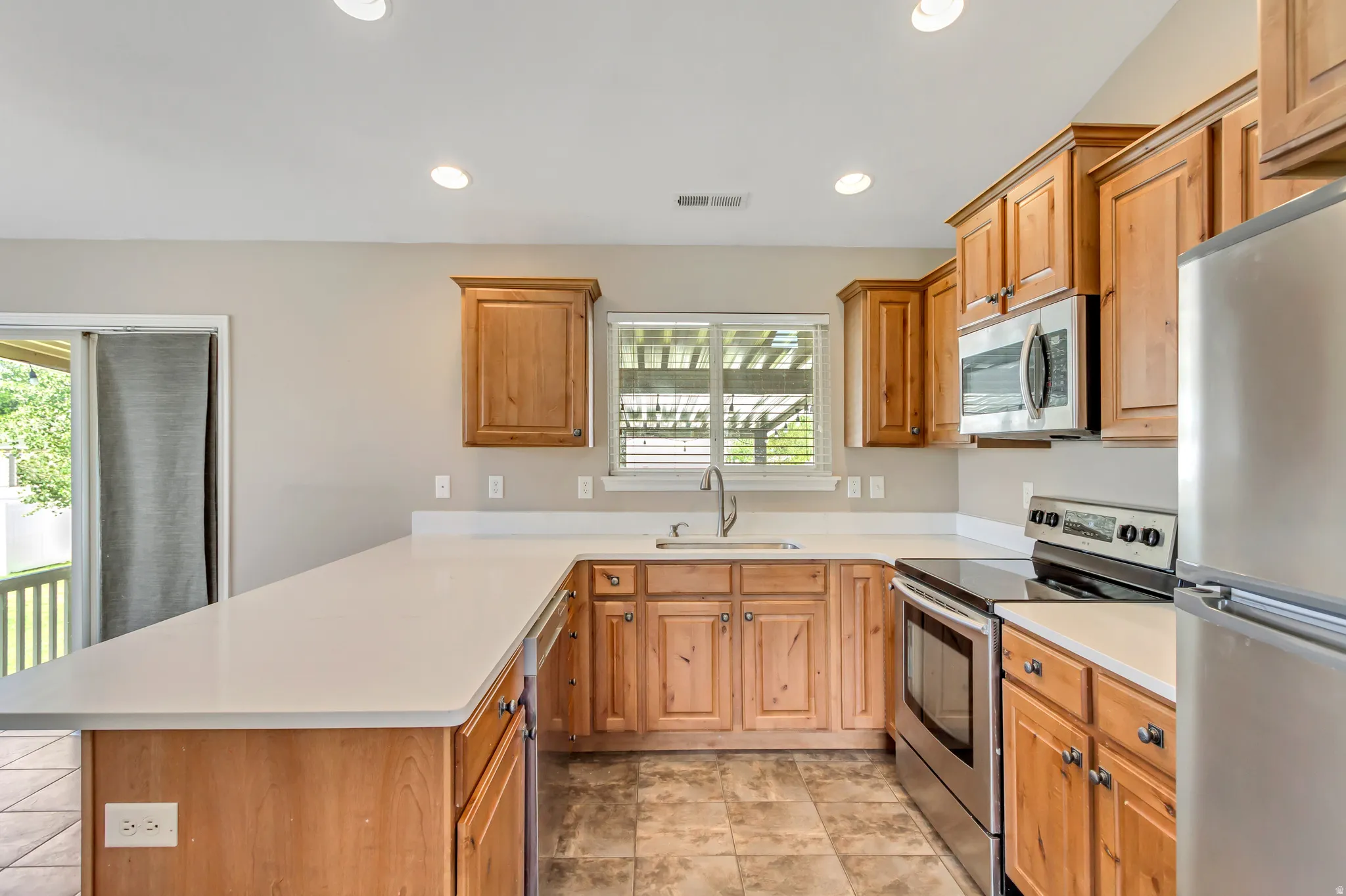 Modern kitchen featuring light wood cabinetry, light-toned countertops, and stainless steel appliances
