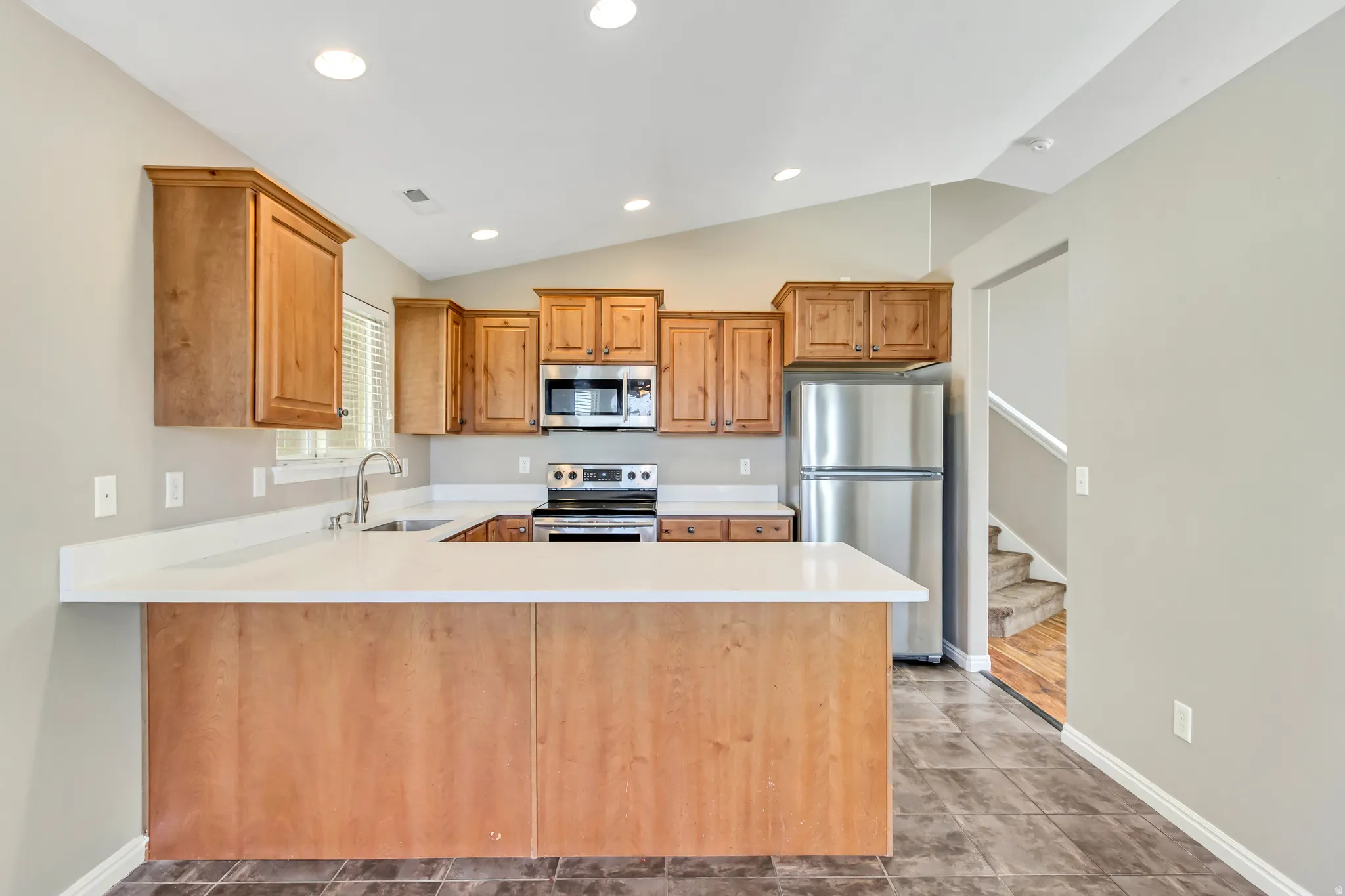 Kitchen featuring light wood cabinetry, stainless steel appliances, solid surface countertops, recessed lighting, and tile flooring
