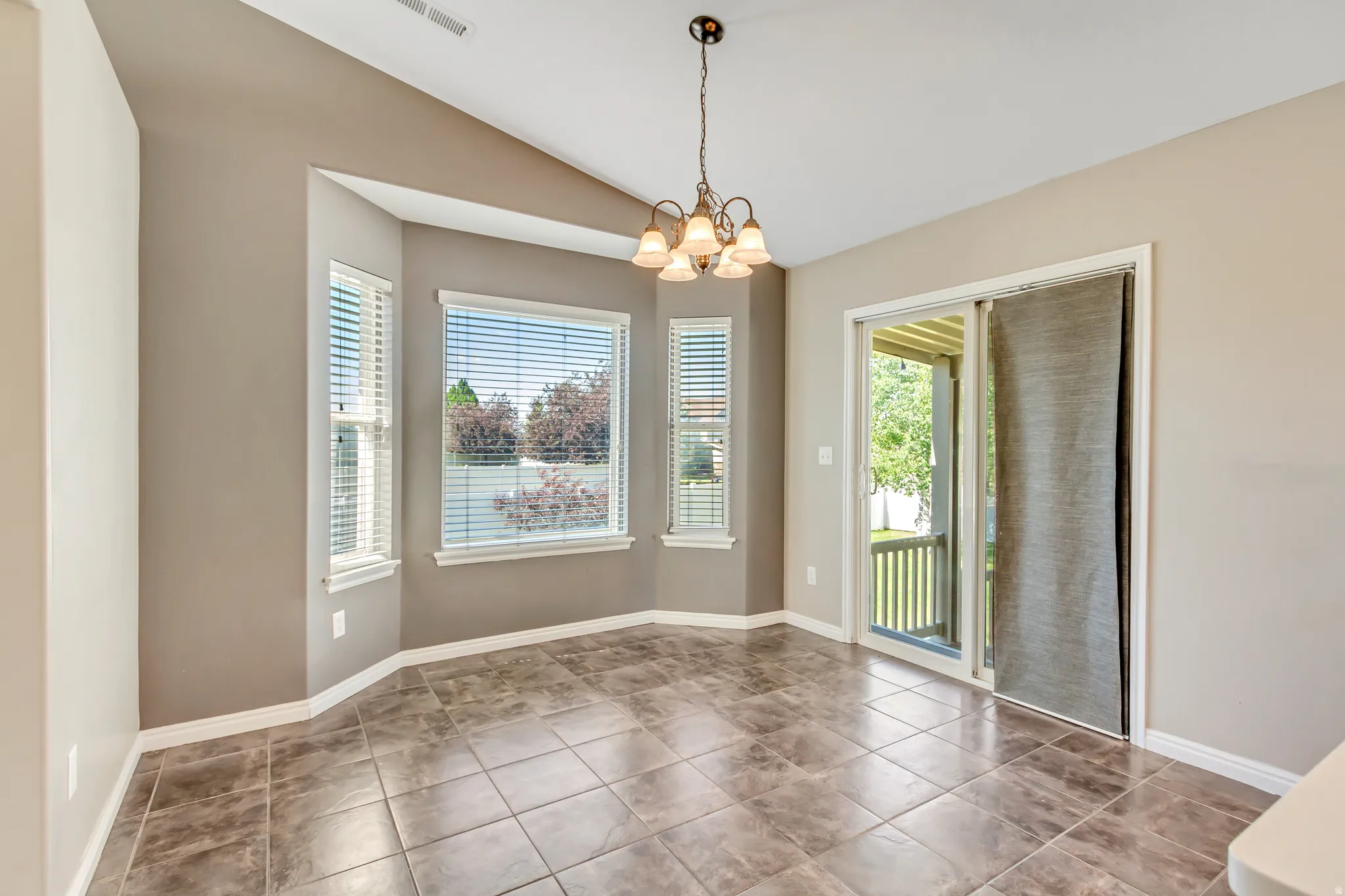Dining area featuring a bay window with multiple panes, a glass sliding door, vaulted ceilings, and tile flooring