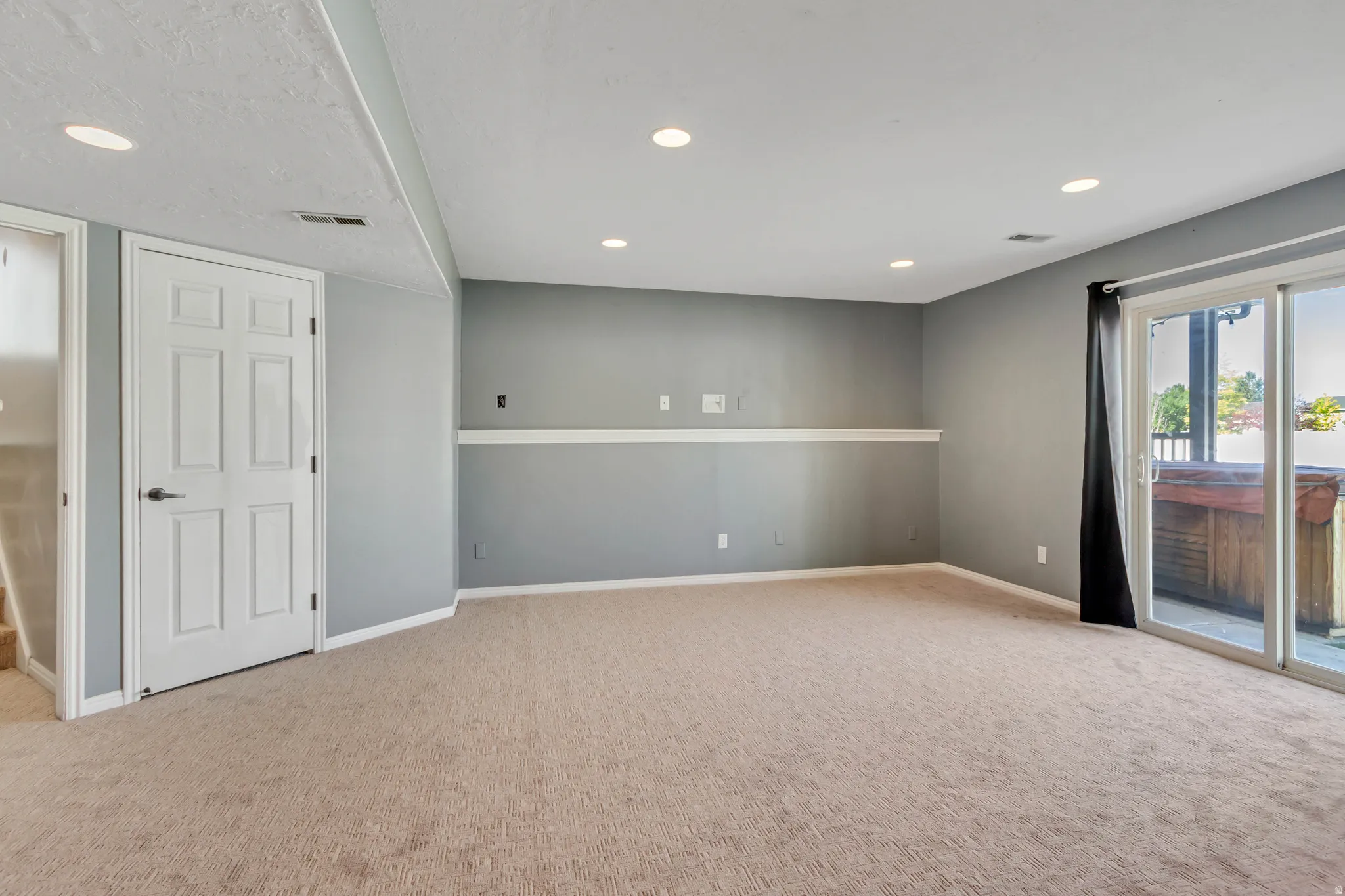 Spacious carpeted room featuring recessed lighting, a sliding glass door providing exterior access, a visible hot tub on the patio, and a paneled interior door