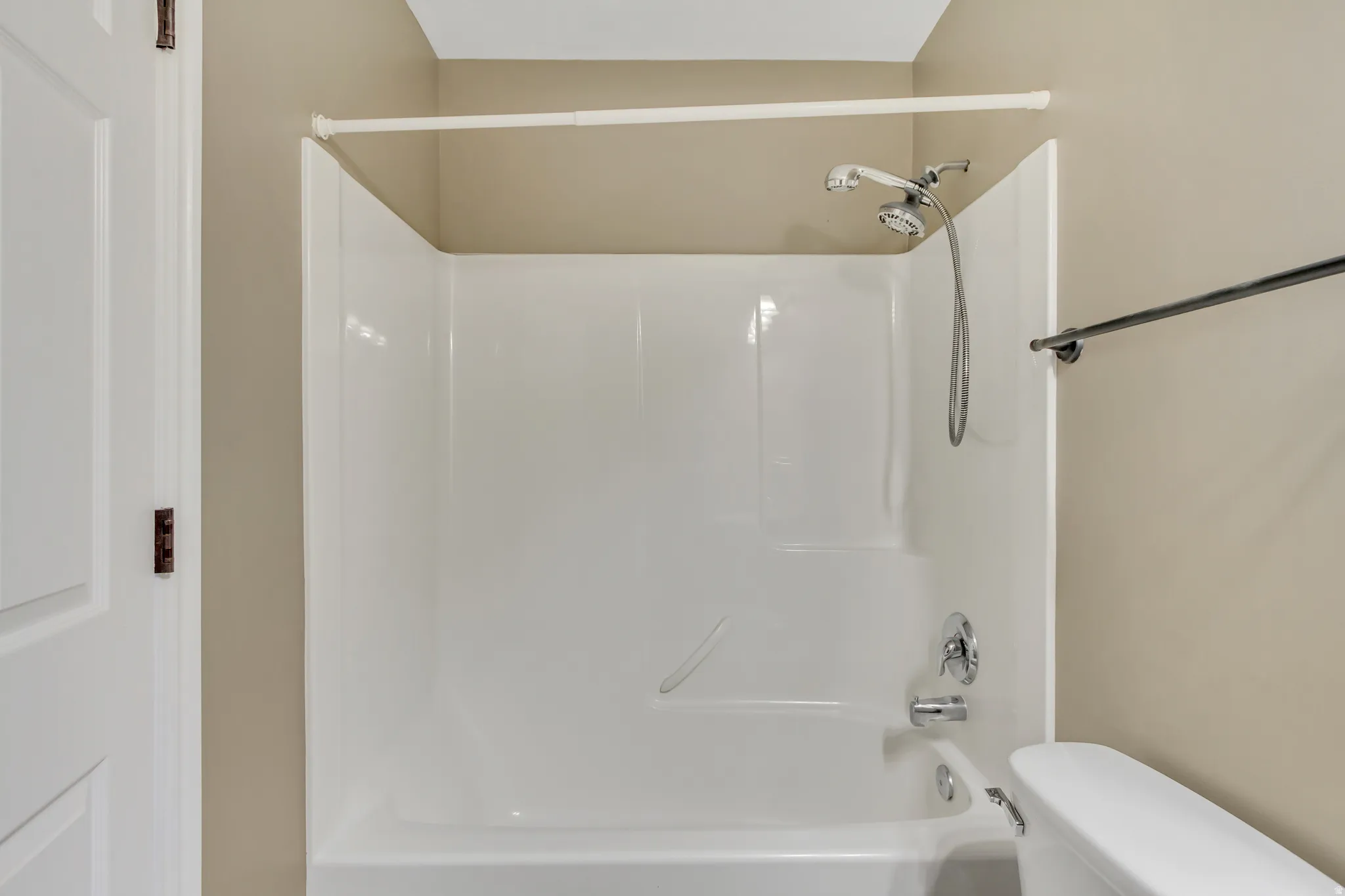 Bathtub and shower combination unit featuring a chrome showerhead with an attached hose, chrome faucet, and a white shower curtain rod