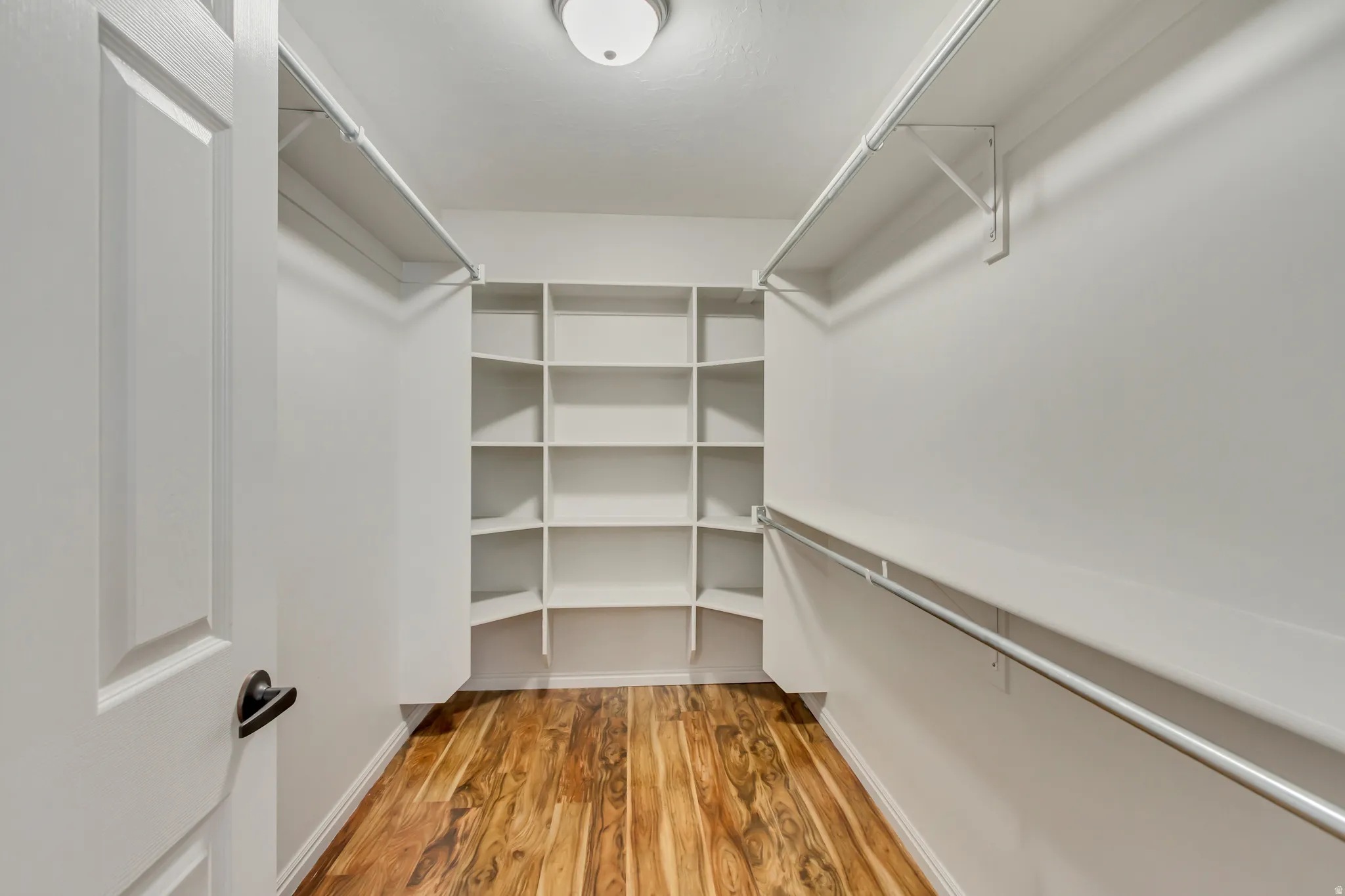 Walk-in closet featuring wood-finish flooring, white walls, built-in shelving, and multiple clothing rods
