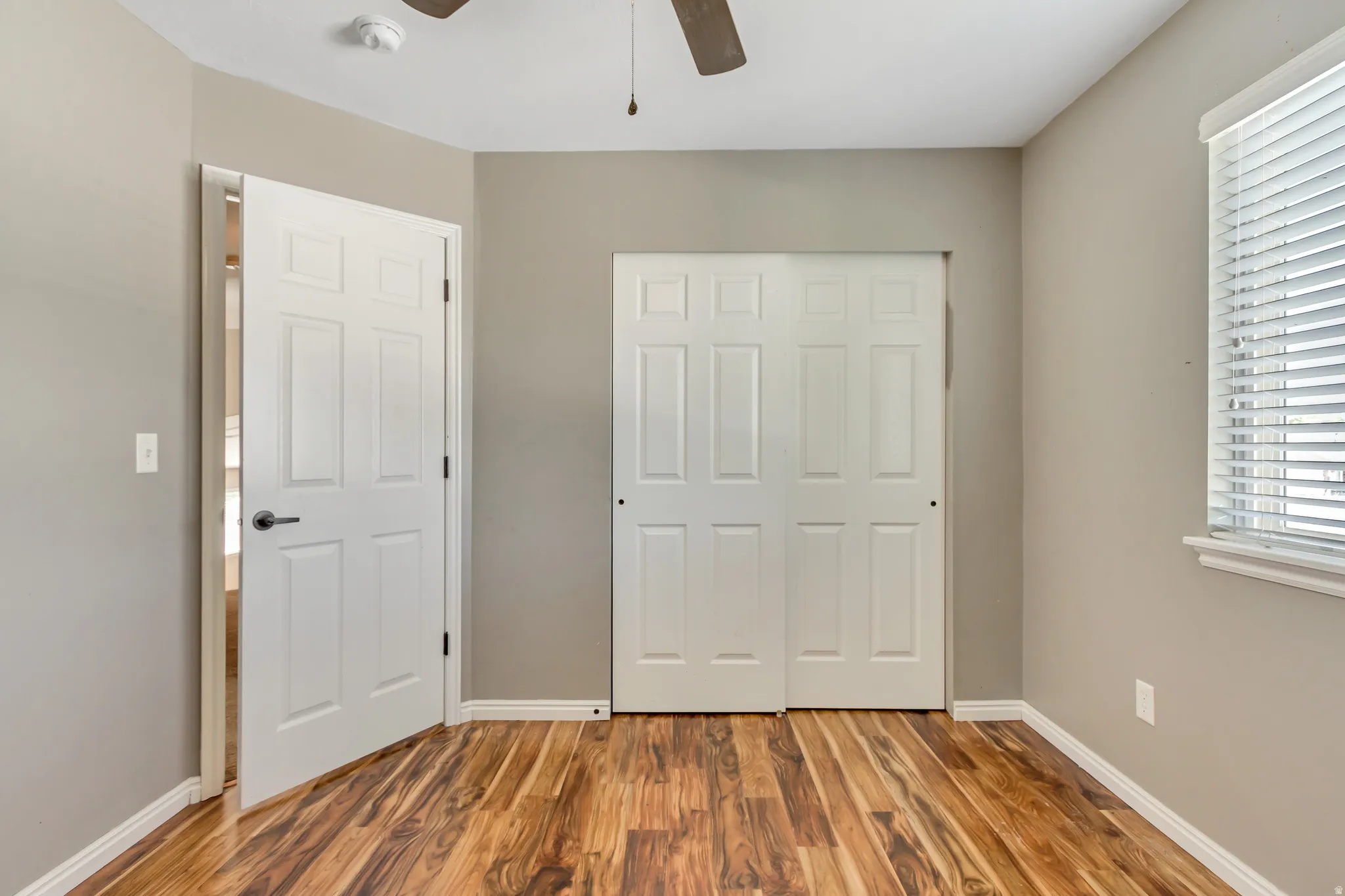Interior room featuring wood-finish flooring, light gray walls, white trim, and a ceiling fan
