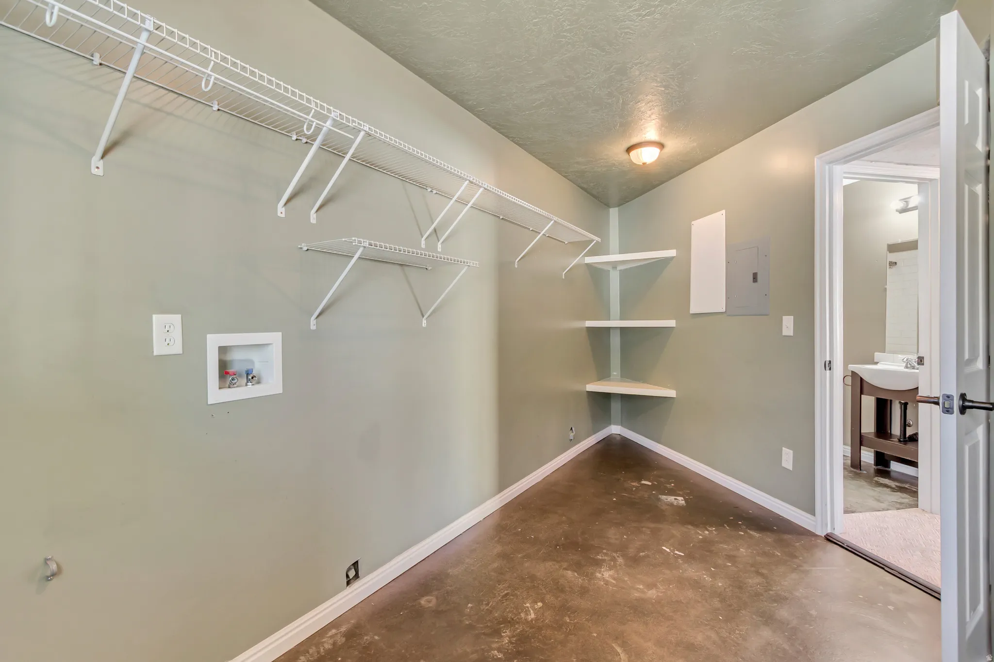 Utility room featuring concrete flooring, wall-mounted wire shelving, corner shelves, a ceiling-mounted light fixture, and a laundry hookup