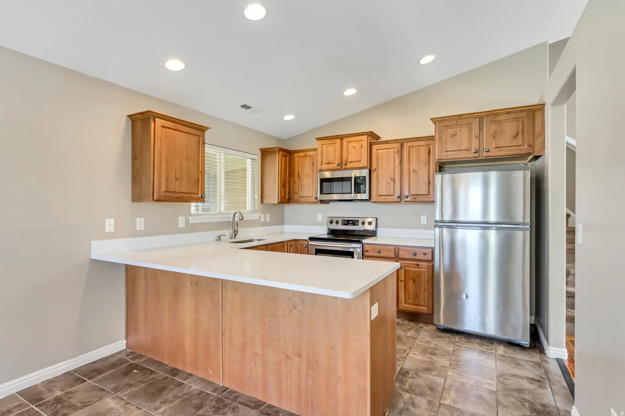 Kitchen featuring wood cabinetry, stainless steel appliances, white countertops, and tile flooring