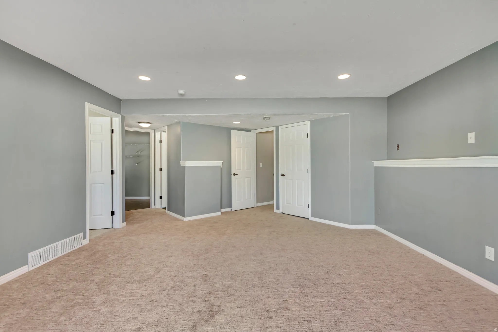 Spacious carpeted room featuring light gray walls, white trim, recessed lighting, and multiple white paneled doors