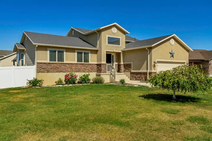 Stucco and stone facade home featuring a two-car garage, front entry stairs, and a partial white vinyl fence