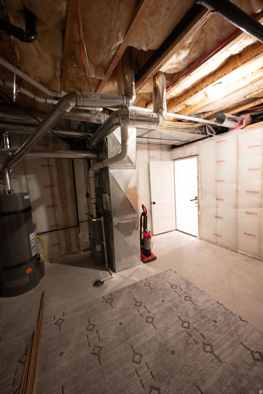 Unfinished basement with concrete flooring, exposed ceiling joists, and visible utility infrastructure, featuring a water heater and HVAC system