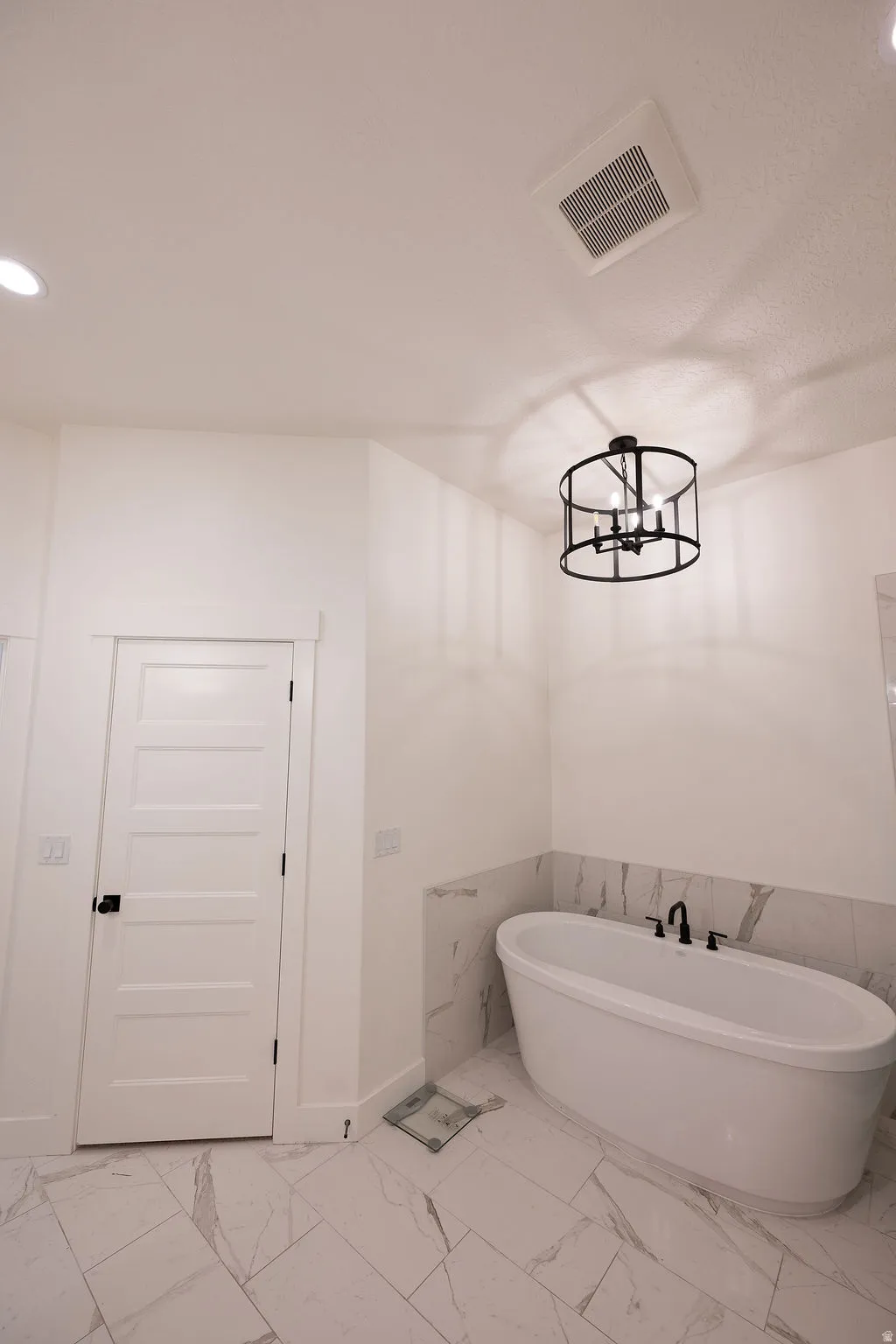 Freestanding soaking tub with matte black fixtures, set against a tiled accent wall