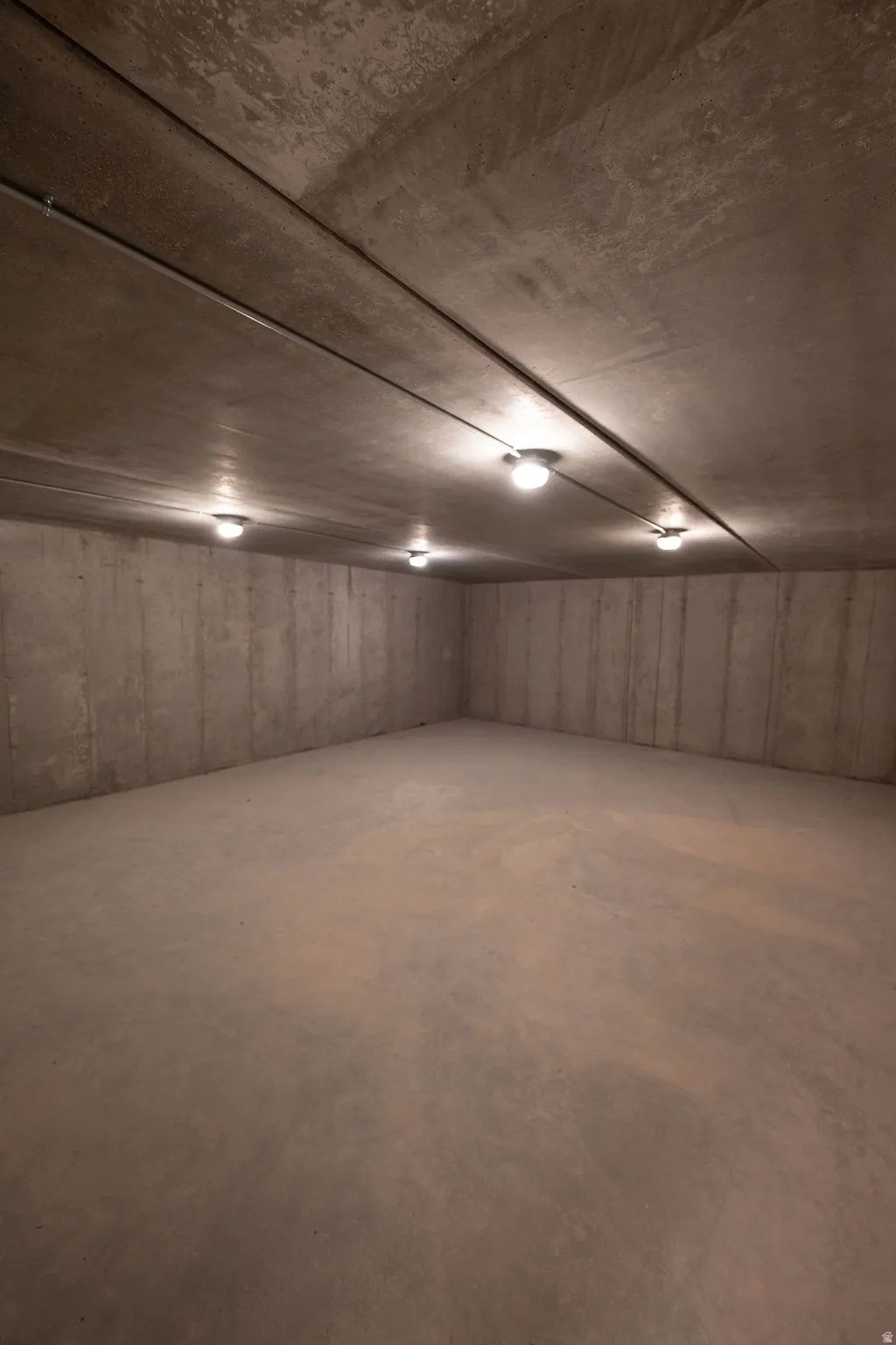 Unfinished concrete basement with overhead track lighting and exposed conduit