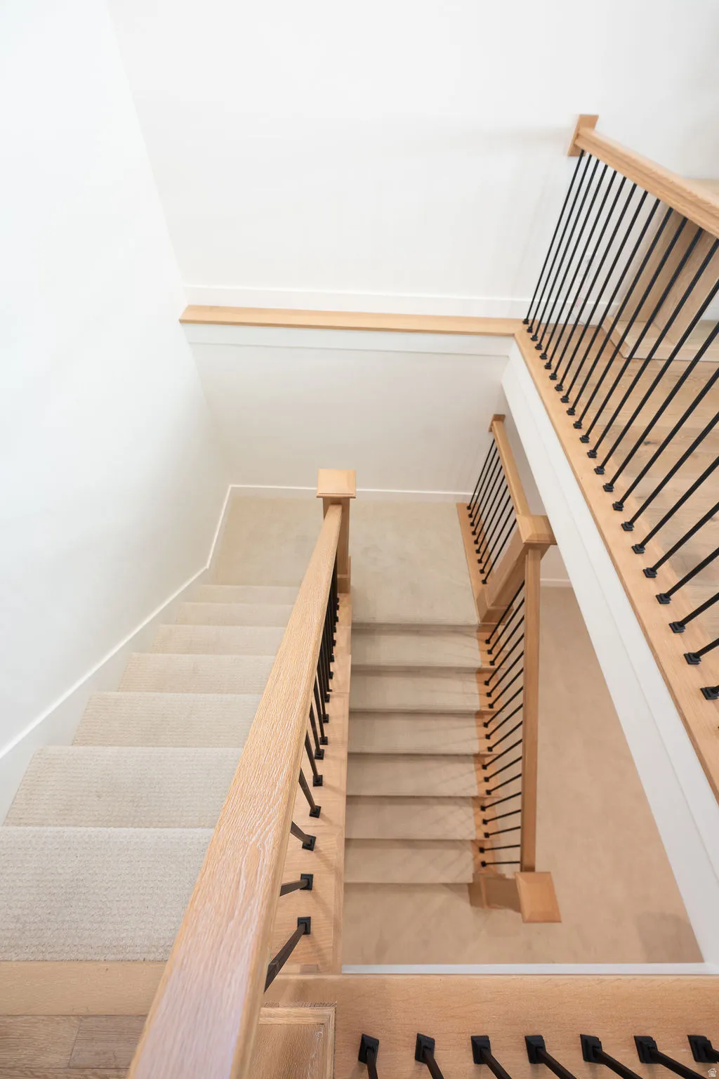 Staircase featuring light wood handrails, black metal balusters, and carpeted treads