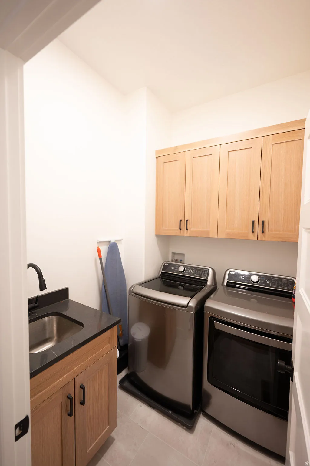 Dedicated laundry area featuring a utility sink with a black faucet, black countertop, light wood cabinetry, and overhead storage cabinets