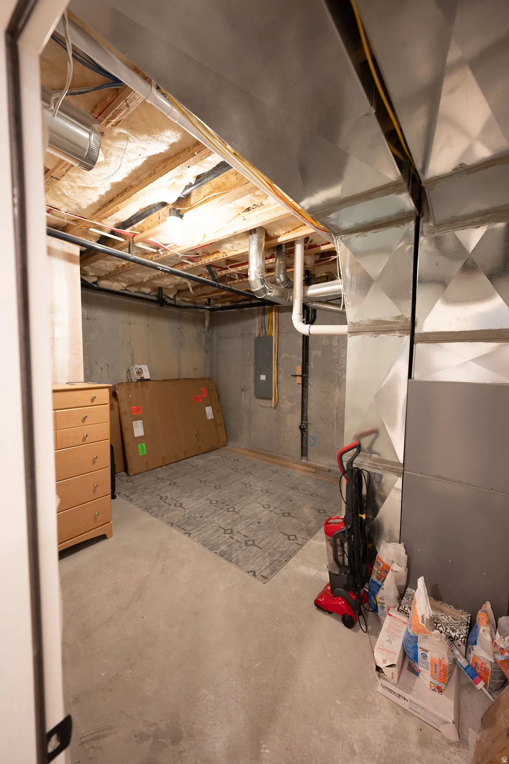 Unfinished basement area featuring exposed ceiling joists, concrete flooring, and visible ductwork