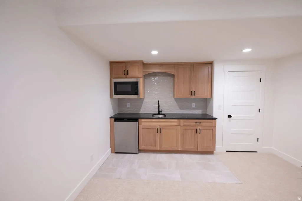 Kitchenette featuring wood-finish cabinetry, dark countertops, a stainless steel microwave, and a compact refrigerator