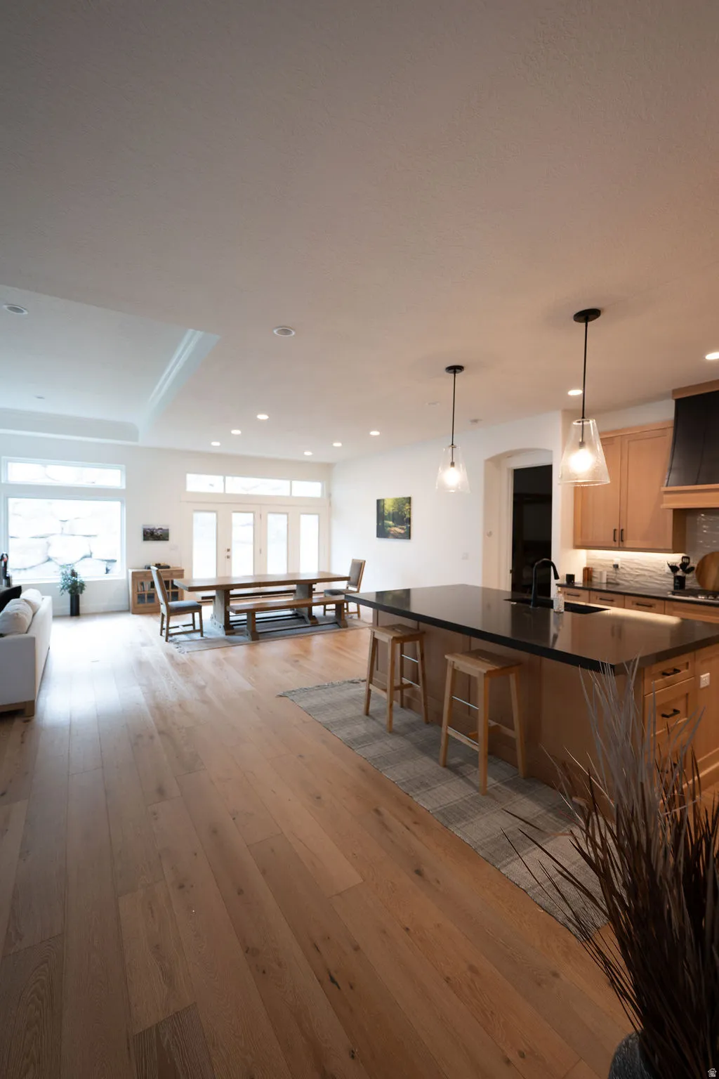Open-concept living space with wide plank wood-finish flooring, recessed lighting, and a tray ceiling