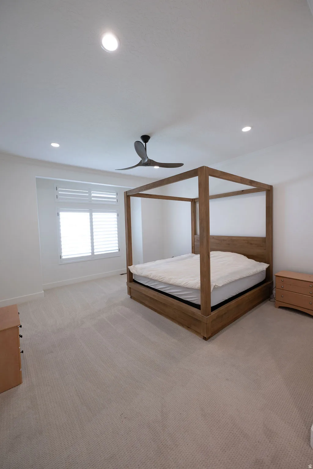Spacious bedroom featuring light-toned carpeting, a ceiling fan, recessed lighting, and a window with plantation shutters