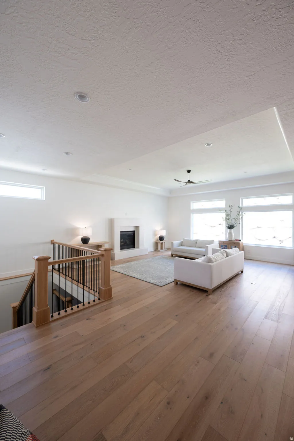 Open-concept living space featuring wood-finish flooring, a contemporary fireplace with a light-colored mantel, and large windows