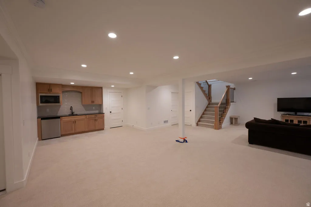 Spacious lower level featuring recessed lighting, light-toned carpeting, a built-in wet bar with wood cabinetry and stainless steel appliances, and a staircase with wood newel posts and glass panels