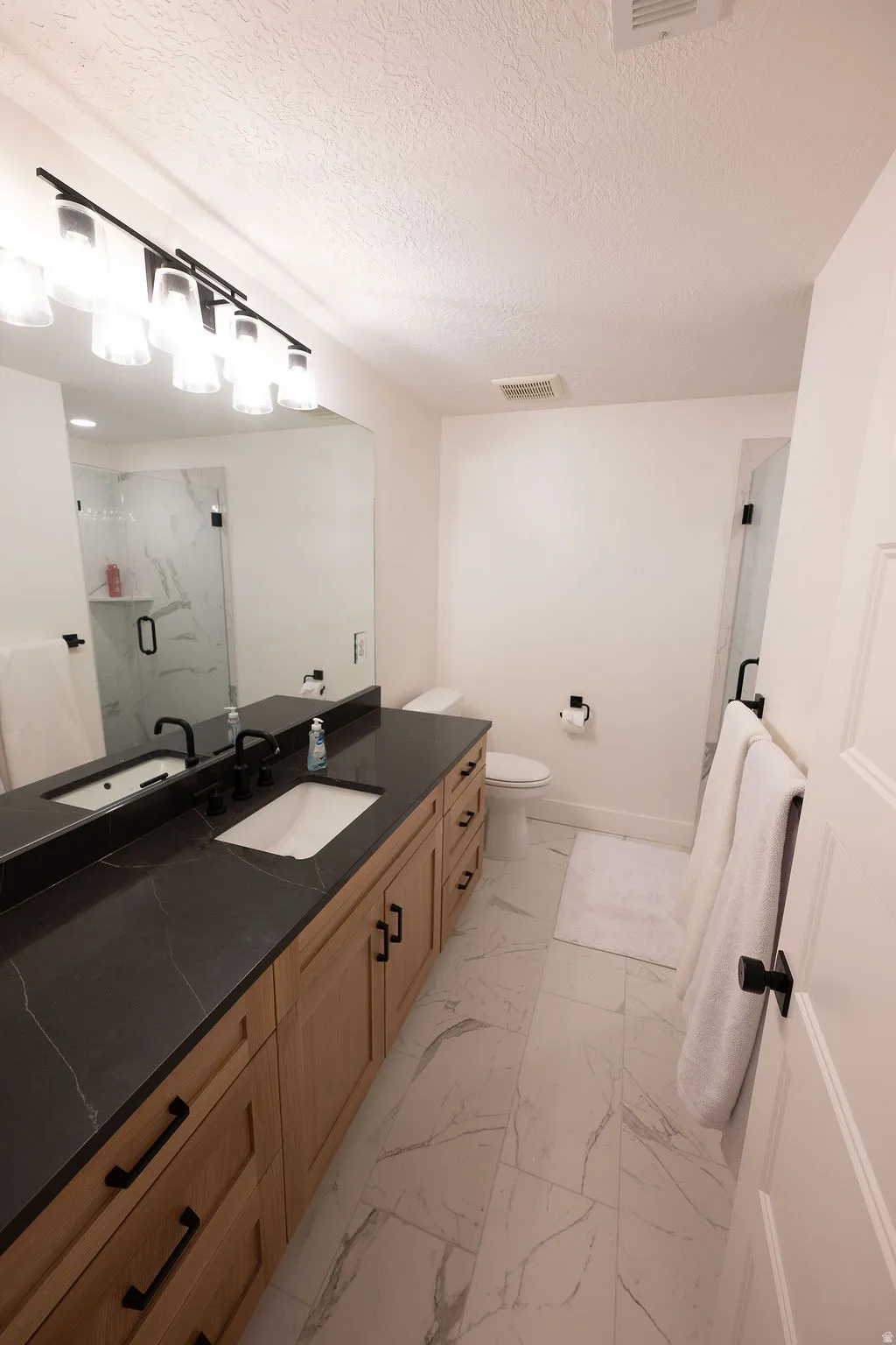Double vanity featuring a black countertop with integrated sinks, wood-finish cabinetry, and matte black hardware