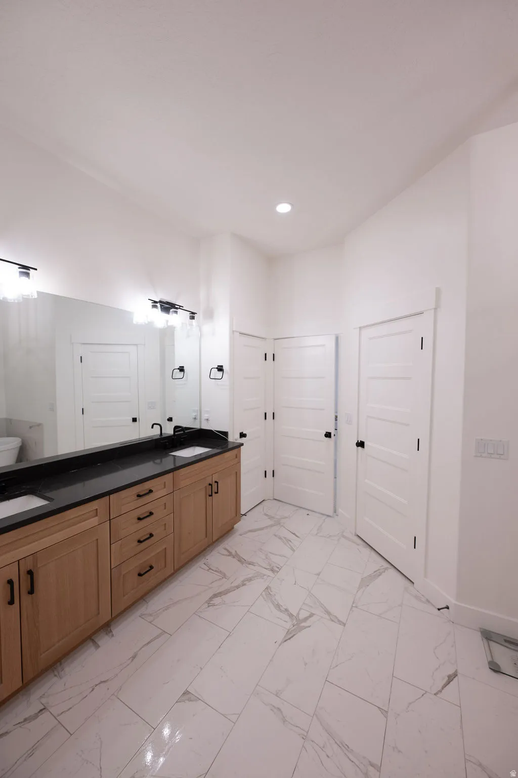 Bathroom featuring a dual vanity with light wood cabinetry and black countertops