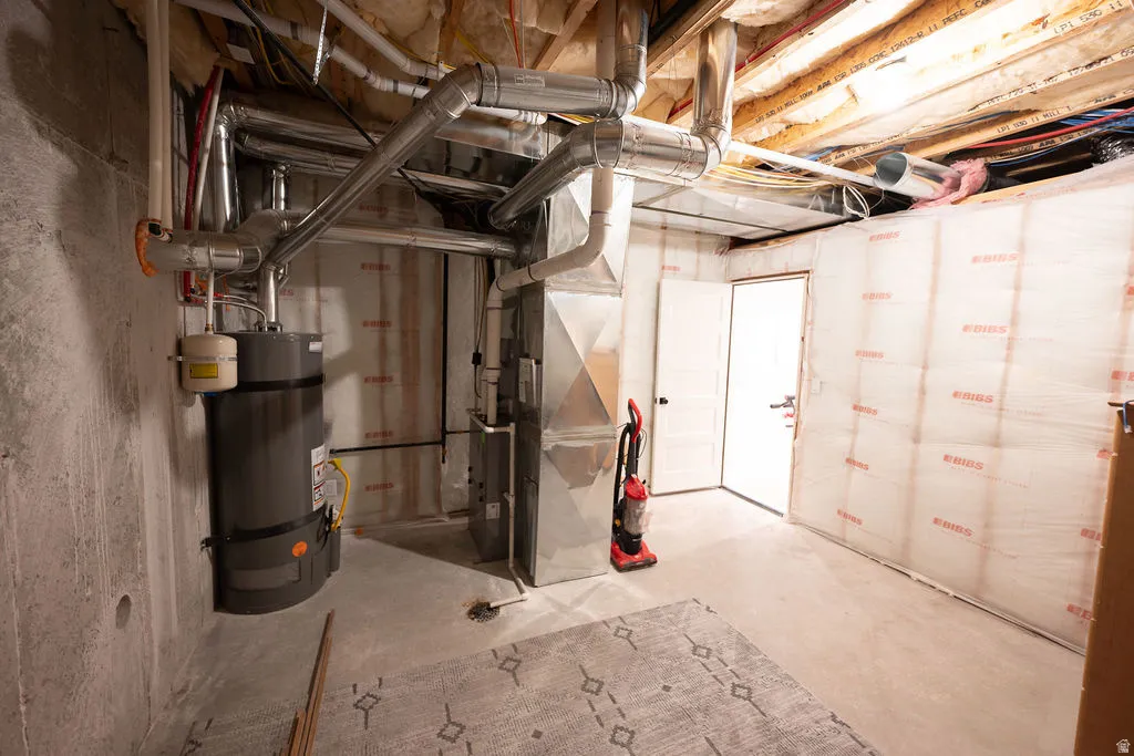 Unfinished basement space featuring a concrete floor, exposed ceiling joists, and a water heater installation