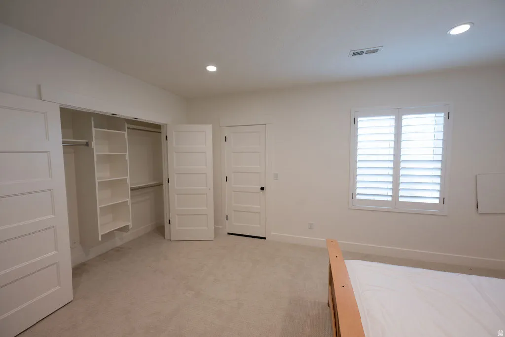 Carpeted room featuring a built-in closet system with shelving and hanging rods, white louvered window shutters, recessed lighting, and a five-panel interior door