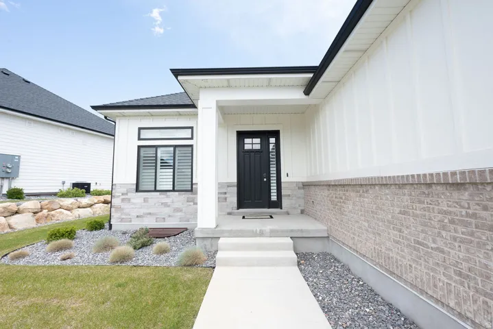 Modern exterior featuring white board and batten siding, light-colored brick veneer, and a black front door with decorative glass inserts
