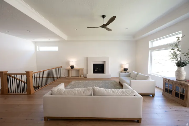 Open-concept living space featuring wood-finish flooring, a contemporary fireplace with a light-toned surround, and a tray ceiling with a modern ceiling fan