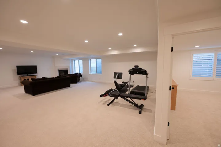 Expansive carpeted room featuring recessed lighting, a fireplace with a stone surround, and multiple windows with white louvered blinds