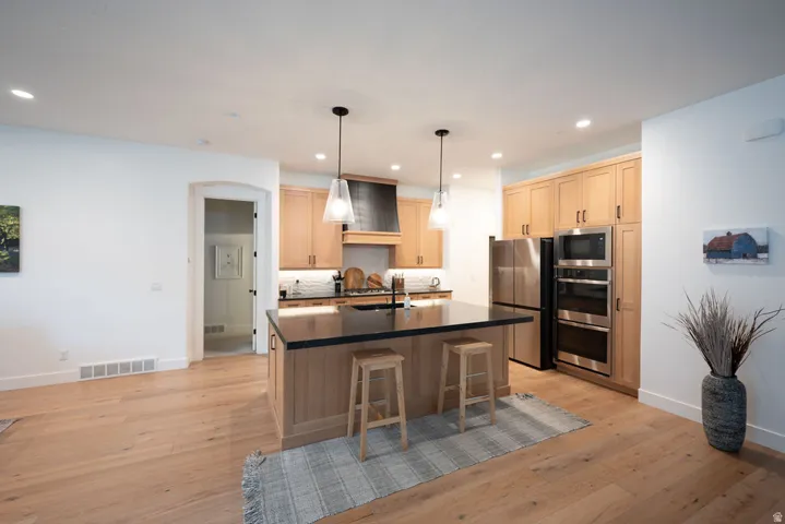 Spacious kitchen featuring an expansive center island with a dark countertop, light wood cabinetry, stainless steel appliances, a tile backsplash, and recessed lighting
