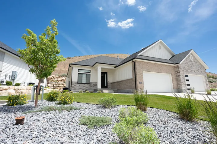 Modern exterior featuring a combination of light brick and stone accents, a dark shingle roof, and a two-car garage with contemporary doors