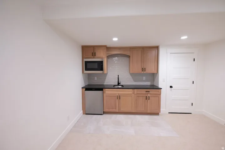 Kitchenette featuring wood-finish cabinetry, dark countertops, a stainless steel microwave, and a compact refrigerator