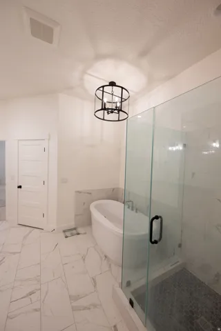 Spacious bathroom featuring a freestanding soaking tub, a walk-in shower with clear glass enclosure and dark hexagonal tile, large-format marble-look floor tiles, and a contemporary black metal chandelier
