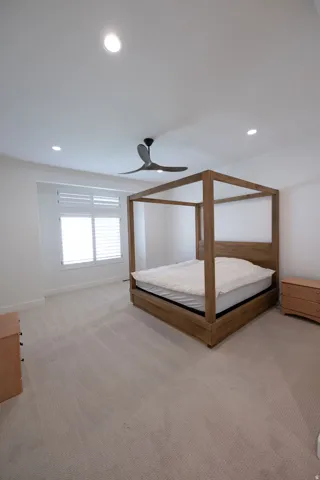 Spacious bedroom featuring light-toned carpeting, a ceiling fan, recessed lighting, and a window with plantation shutters