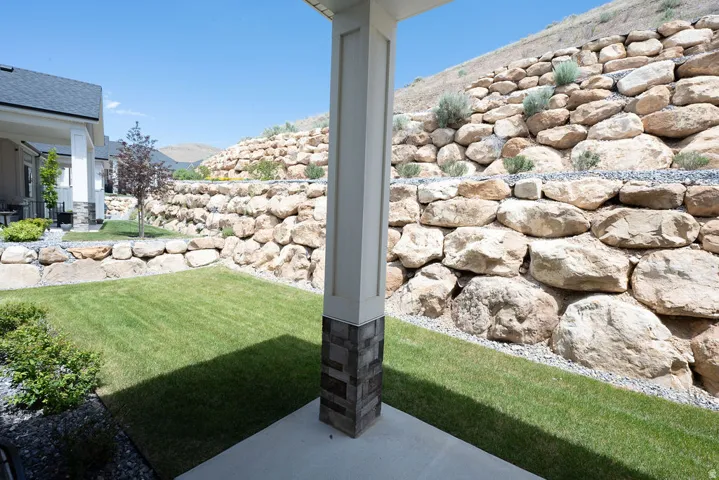 Backyard featuring a paved patio area, green lawn, and tiered rock retaining walls