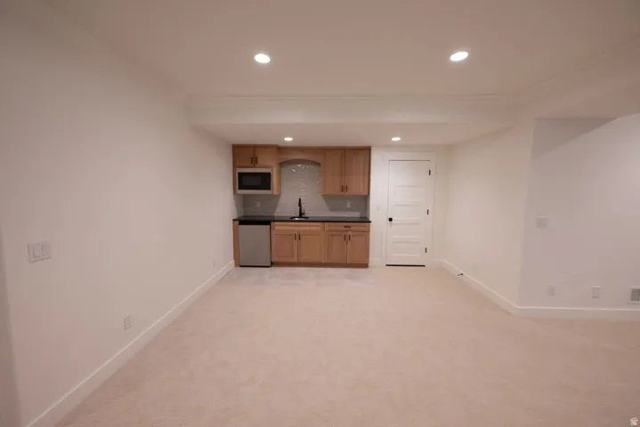 Lower level featuring a wet bar with wood cabinetry, a stainless steel microwave, a stainless steel beverage refrigerator, and a dark stone countertop