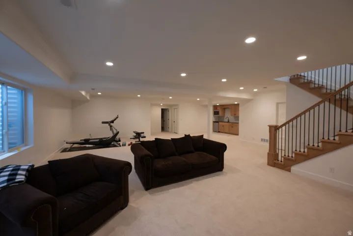 Spacious lower level featuring plush carpeting, recessed lighting, a built-in wet bar with wood cabinetry and stainless steel appliances, a window with a security grate, and a wood staircase with black iron balusters