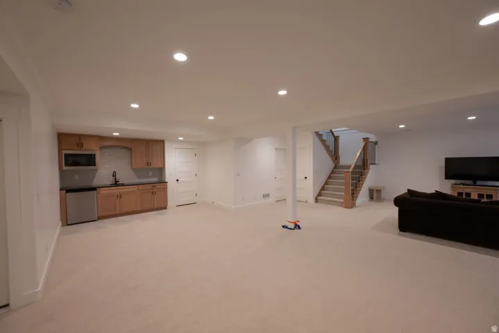 Spacious lower level featuring recessed lighting, light-toned carpeting, a built-in wet bar with wood cabinetry and stainless steel appliances, and a staircase with wood newel posts and glass panels
