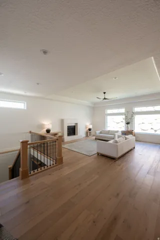 Spacious living area featuring wood-finish flooring, a fireplace with a light-toned surround, a coffered ceiling with recessed lighting, and a ceiling fan
