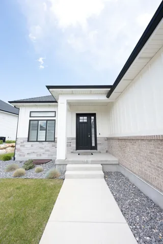 Modern architectural exterior featuring a black entry door with frosted glass, board and batten siding, stone veneer, and dark-trimmed windows